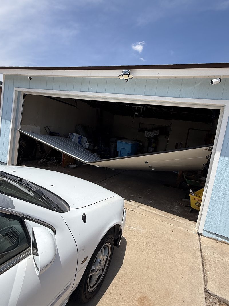 A garage door that has collapsed inward, with a car parked in the driveway unable to enter