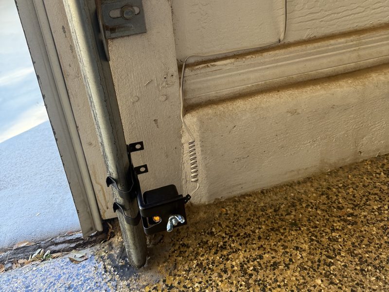 A garage door safety sensor mounted low on the track with its indicator light on